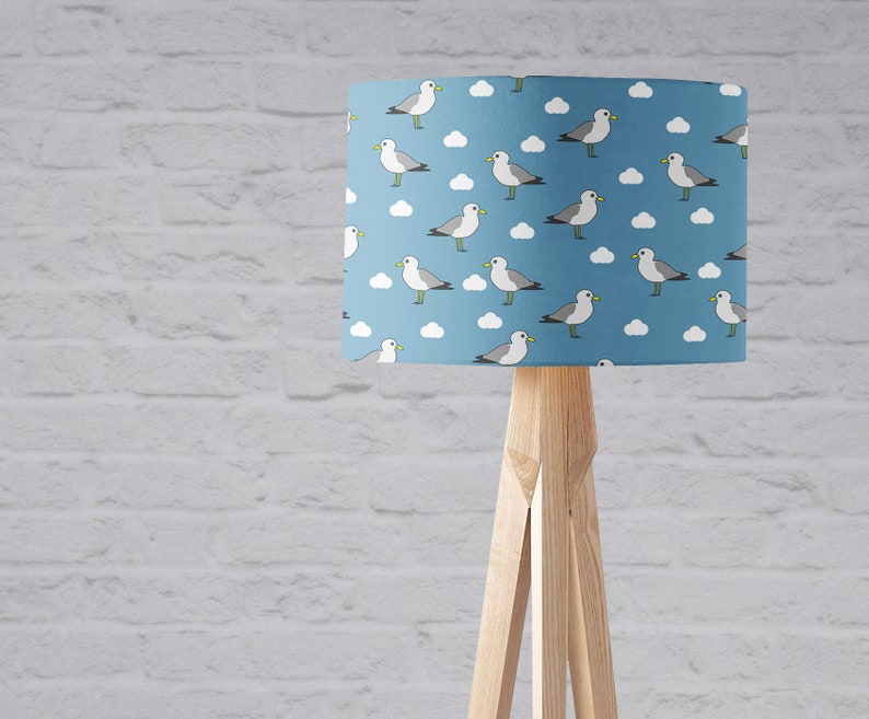 May include: A blue lampshade with a white and gray seagull pattern. The lampshade is on a wooden tripod stand.