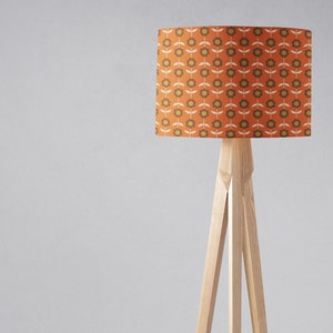 Puede incluir: Una l&aacute;mpara de pie con una base de tr&iacute;pode de madera y una pantalla cil&iacute;ndrica con un patr&oacute;n floral retro en tonos naranja, marr&oacute;n y amarillo.