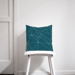 Puede incluir: Almohada azul turquesa con un patr&oacute;n geom&eacute;trico blanco. La almohada est&aacute; sentada en una silla blanca.