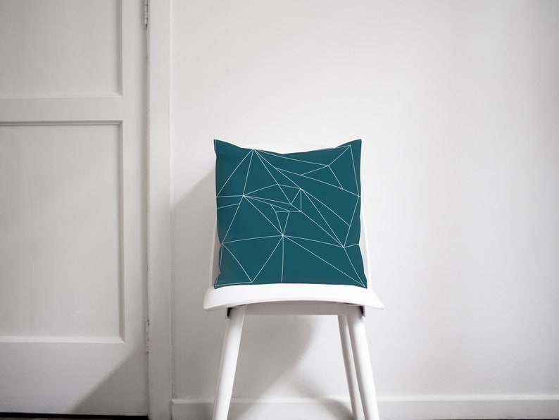 Puede incluir: Almohada azul turquesa con un patr&oacute;n geom&eacute;trico blanco. La almohada est&aacute; sentada en una silla blanca.