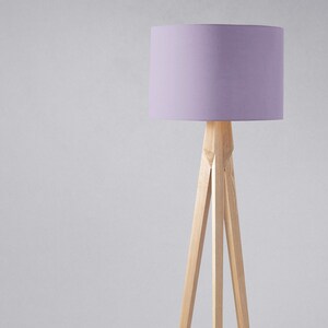 May include: A tripod floor lamp with a light purple fabric lampshade. The lamp is made of natural wood.