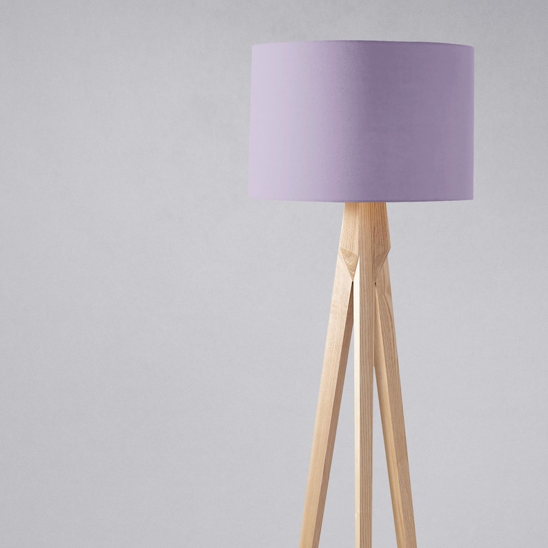 May include: A tripod floor lamp with a light purple fabric lampshade. The lamp is made of natural wood.