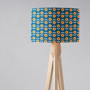 May include: A wooden tripod floor lamp with a blue lampshade featuring a repeating pattern of yellow flowers with red centers.