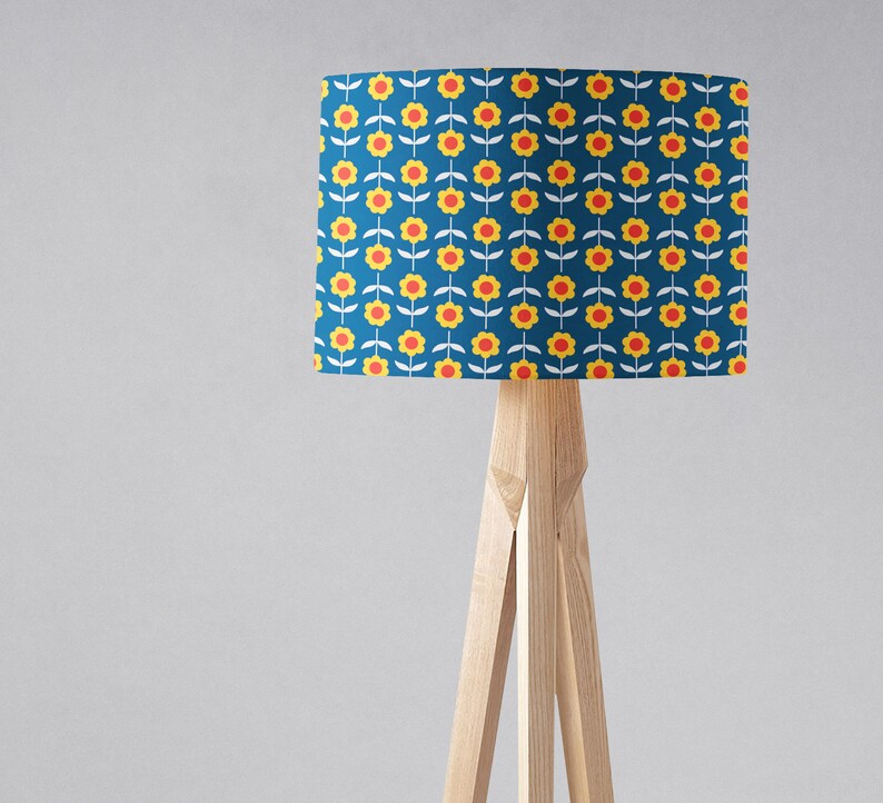 May include: A wooden tripod floor lamp with a blue lampshade featuring a repeating pattern of yellow flowers with red centers.