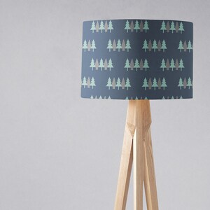 May include: A floor lamp with a blue lampshade featuring a repeating pattern of green and brown trees. The lamp has a wooden tripod base.