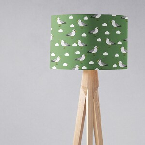 May include: A green lampshade with a white and gray seagull pattern. The lampshade is on a wooden tripod stand.