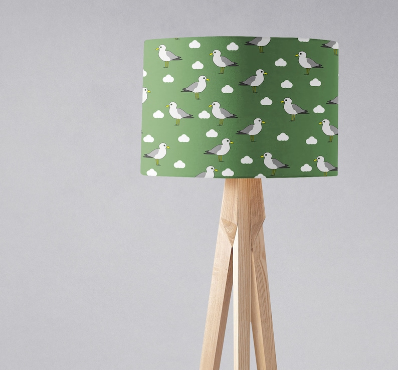 May include: A green lampshade with a white and gray seagull pattern. The lampshade is on a wooden tripod stand.
