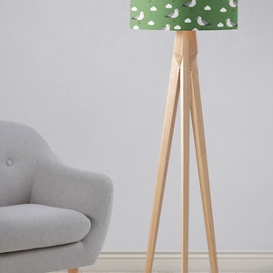 May include: A green floor lamp with a white and gray seagull pattern lampshade. The lamp has a wooden tripod base.