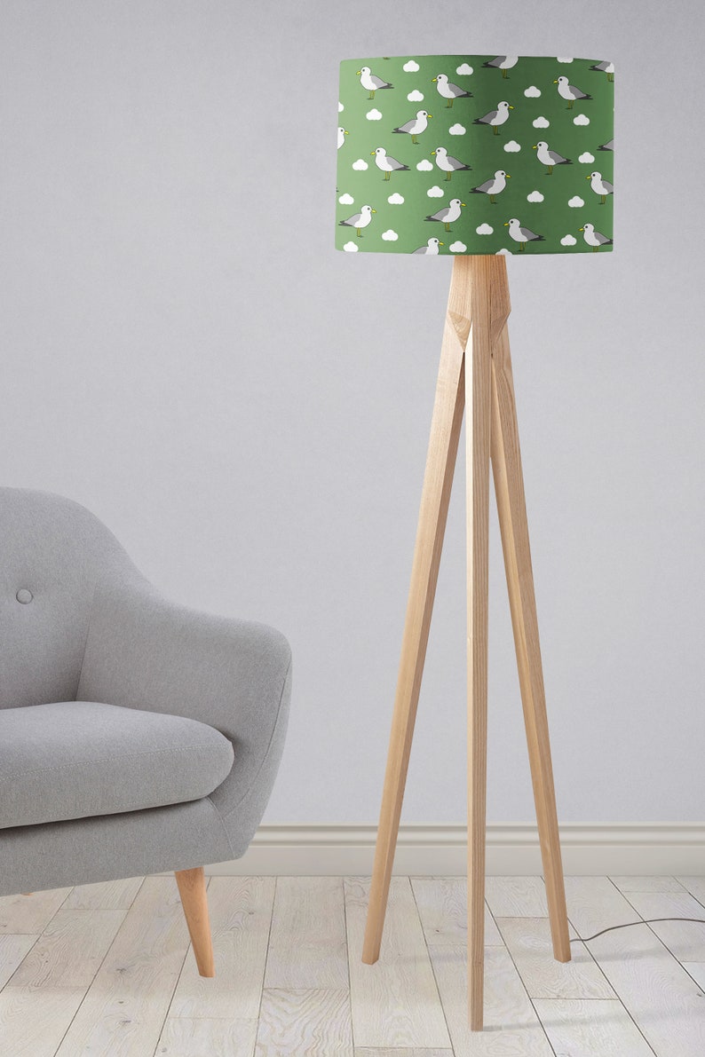 May include: A green floor lamp with a white and gray seagull pattern lampshade. The lamp has a wooden tripod base.