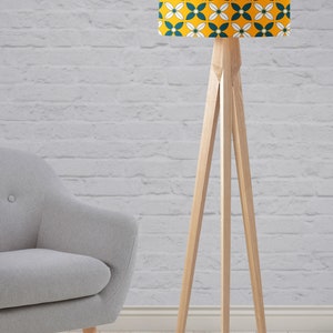 May include: A wooden floor lamp with a tripod base and a yellow and teal patterned lampshade. The lampshade has a geometric pattern of white flowers and teal leaves.