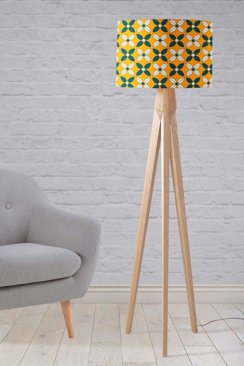 May include: A wooden floor lamp with a tripod base and a yellow and teal patterned lampshade. The lampshade has a geometric pattern of white flowers and teal leaves.