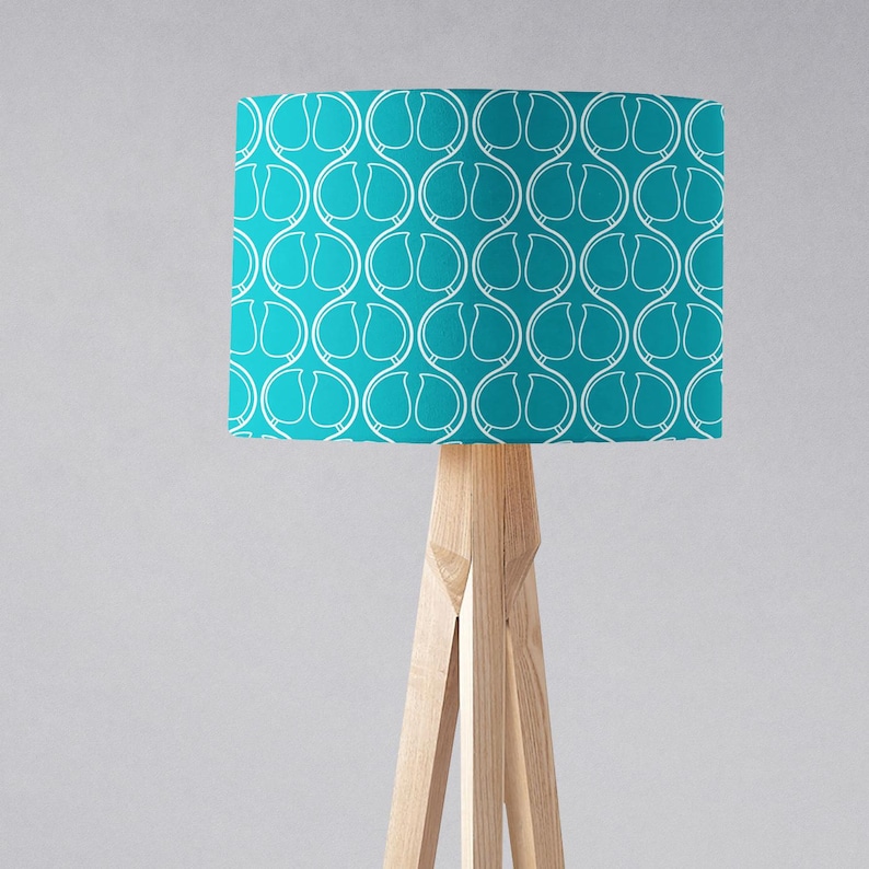 May include: A teal blue floor lamp with a white geometric pattern on the lampshade. The lamp has a tripod base made of natural wood.