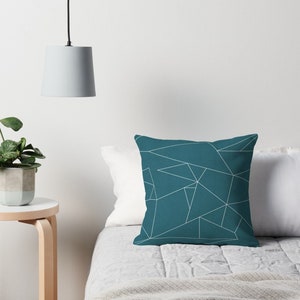 Puede incluir: Almohada de color azul turquesa con un patr&oacute;n geom&eacute;trico blanco. La almohada est&aacute; sobre una cama con una manta blanca y una colcha.