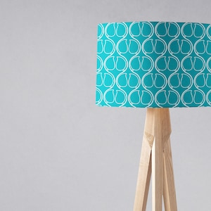 May include: A turquoise floor lamp with a white geometric pattern on the lampshade. The lamp has a wooden tripod base.