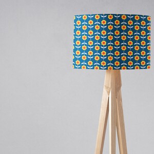 May include: A floor lamp with a blue lampshade featuring a repeating pattern of yellow flowers with red centers. The lampshade is cylindrical and the lamp has a wooden tripod base.