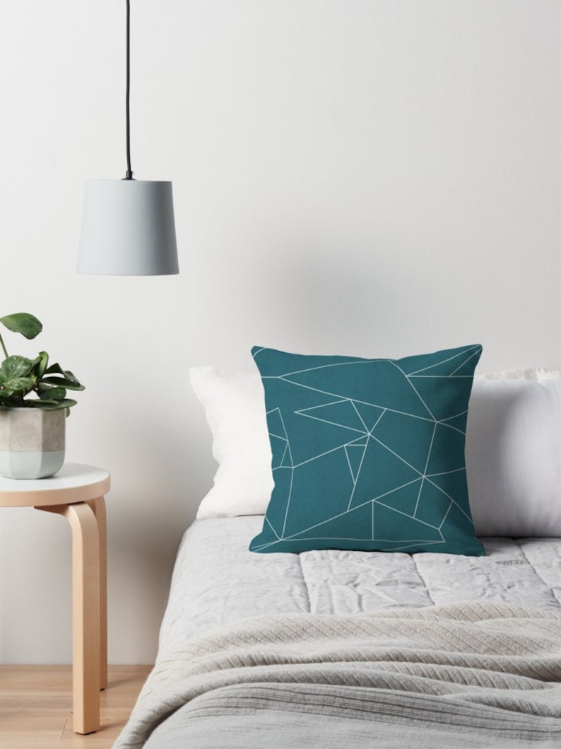 Puede incluir: Almohada de color azul turquesa con un patr&oacute;n geom&eacute;trico blanco. La almohada est&aacute; sobre una cama con una manta blanca y una colcha.
