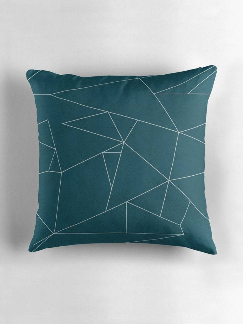Puede incluir: Coj&iacute;n de tiro azul teal con un patr&oacute;n geom&eacute;trico blanco. El patr&oacute;n est&aacute; formado por tri&aacute;ngulos y l&iacute;neas.