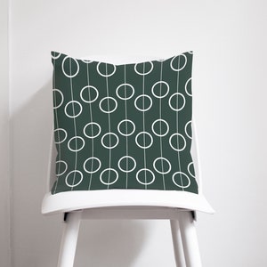 May include: A dark green throw pillow with a white geometric pattern of circles and lines. The pillow is sitting on a white chair.