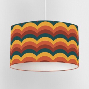 May include: A retro-style lampshade with a repeating wave pattern in shades of teal, orange, yellow, and rust. The lampshade is cylindrical with a white interior and hangs from a white cord. The design evokes a vintage aesthetic.