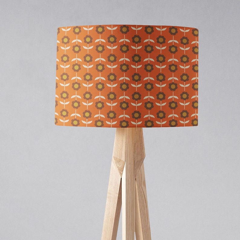 Puede incluir: Una l&aacute;mpara de pie con una base de tr&iacute;pode de madera y una pantalla cil&iacute;ndrica con un patr&oacute;n floral retro en tonos naranja, marr&oacute;n y blanco.
