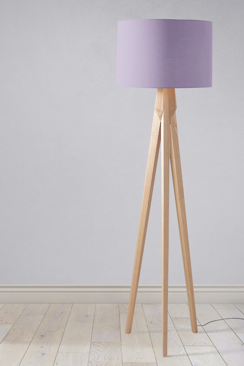 May include: A tripod floor lamp with a light purple fabric lampshade. The lamp is made of natural wood and has a simple, modern design.