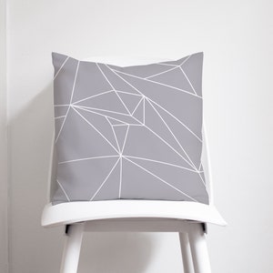 May include: A grey throw pillow with a white geometric pattern. The pillow is sitting on a white chair.