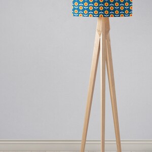 May include: A wooden tripod floor lamp with a blue lampshade featuring a yellow and red floral pattern.