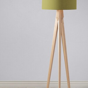 May include: A wooden tripod floor lamp with a green fabric lampshade. The lamp is standing on a light wood floor.