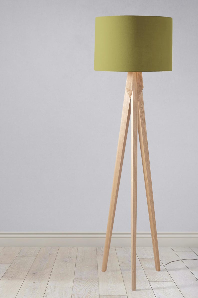 May include: A wooden tripod floor lamp with a green fabric lampshade. The lamp is standing on a light wood floor.
