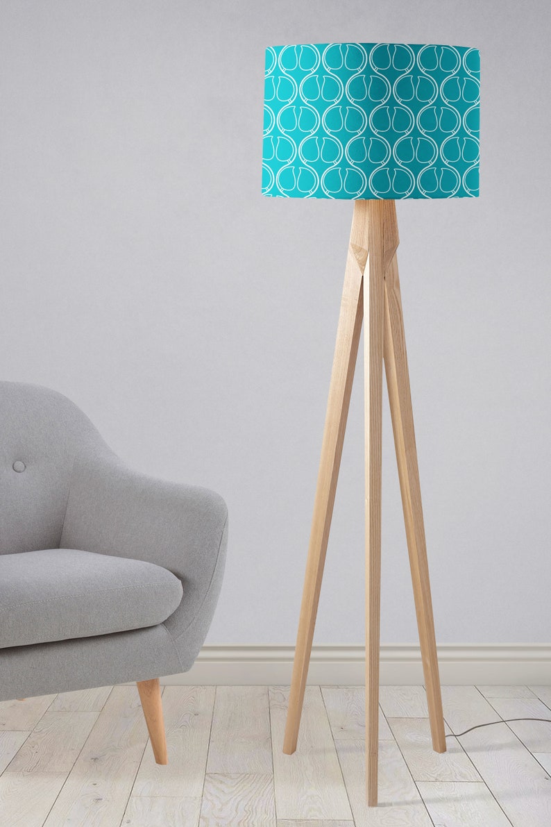 May include: A turquoise floor lamp with a white geometric pattern on the lampshade. The lamp has a wooden tripod base.