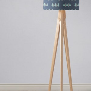 May include: A wooden tripod floor lamp with a blue lampshade featuring a repeating pattern of green and brown stylized trees.