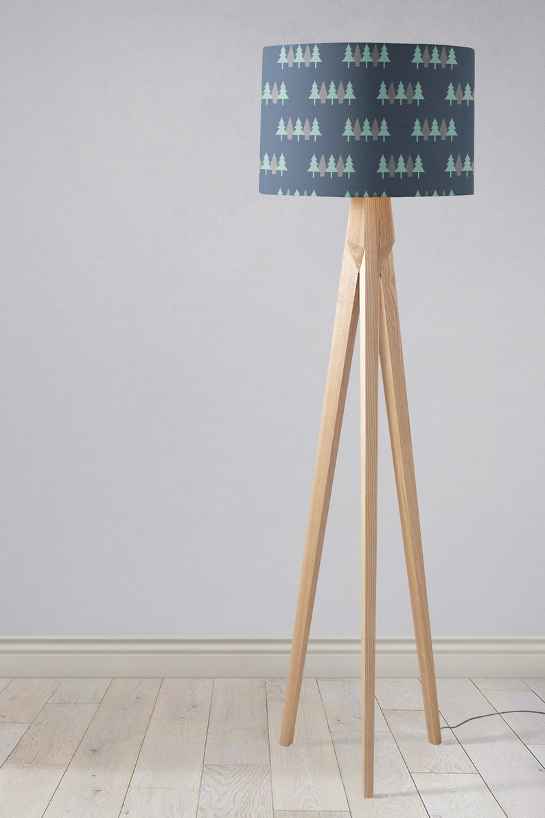 May include: A wooden tripod floor lamp with a blue lampshade featuring a repeating pattern of green and brown stylized trees.
