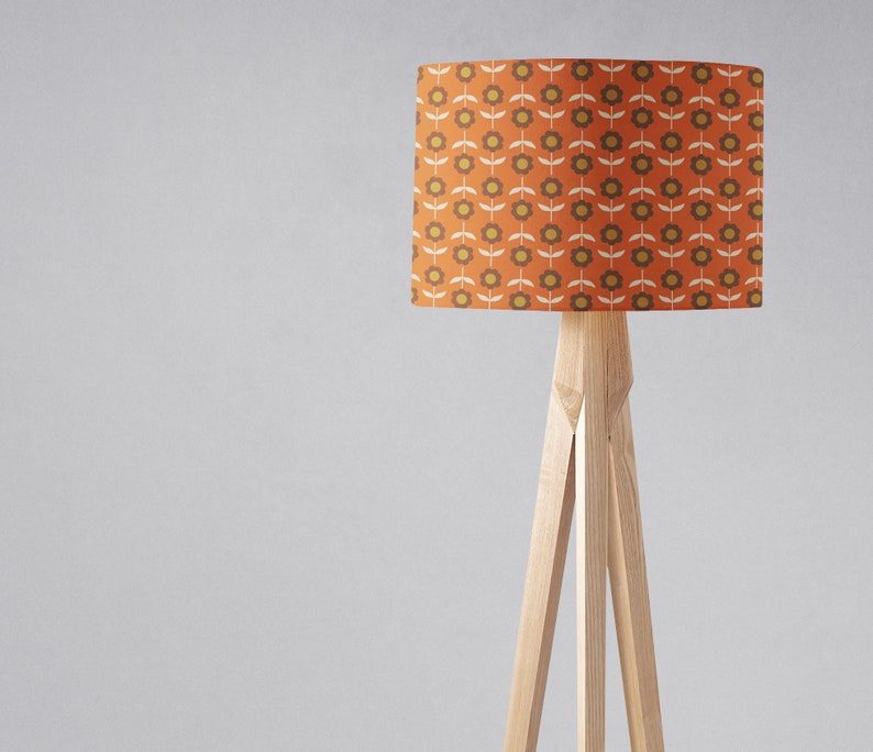 Puede incluir: Una l&aacute;mpara de pie con una base de tr&iacute;pode de madera y una pantalla cil&iacute;ndrica con un patr&oacute;n floral retro en tonos naranja, marr&oacute;n y amarillo.