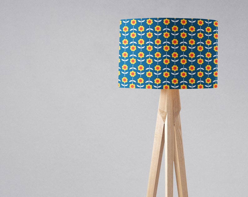 May include: A floor lamp with a blue lampshade featuring a repeating pattern of yellow flowers with red centers. The lampshade is cylindrical and the lamp has a wooden tripod base.