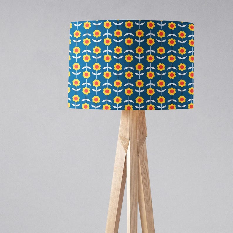 May include: A blue floor lamp with a white wooden tripod base. The lampshade has a repeating pattern of yellow and orange flowers on a blue background.