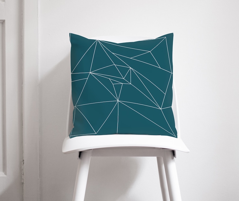Puede incluir: Coj&iacute;n de tiro azul teal con un patr&oacute;n geom&eacute;trico blanco. El coj&iacute;n est&aacute; sentado en una silla blanca.