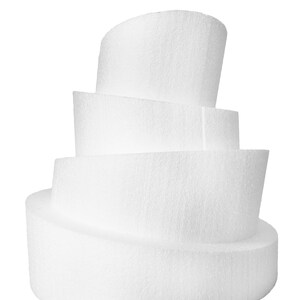 May include: A white, multi-tiered foam cake form with a textured surface. The form has four layers, each with a curved or rounded shape, creating a unique design. The layers are stacked on top of each other, with the largest at the bottom.