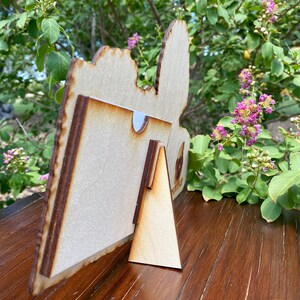 K&ouml;nnte beinhalten: Ein Bilderrahmen aus Holz mit einem ausgeschnittenen Design. Der Rahmen hat einen St&auml;nder und ist aus hellem braunem Holz.
