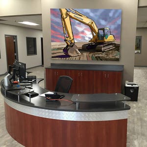 K&ouml;nnte beinhalten: Ein gelber Bagger mit der Aufschrift "KOMATSU" an der Seite ist in einem Gem&auml;lde an einer Wand in einem Gesch&auml;ftsb&uuml;ro zu sehen. Der Bagger gr&auml;bt im Dreck. Das Gem&auml;lde befindet sich &uuml;ber einem dunklen Holzkasten mit einem geschwungenen Empfangstresen davor.
