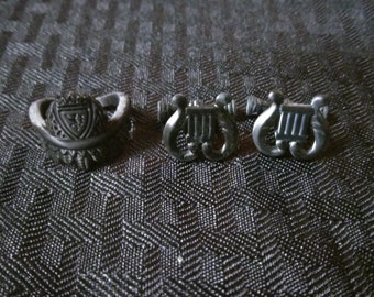 May include: Three silver rings with different designs. The first ring features a shield with a crest. The second and third rings feature a lyre design.