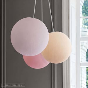 Könnte beinhalten: Drei runde Stoffpendelleuchten in Rosa, Hellrosa und Beige, die an einer weißen Decke hängen.