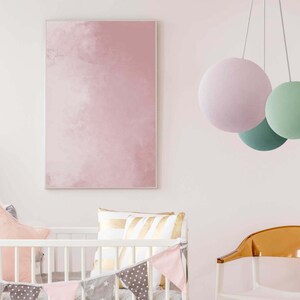 May include: A white crib with a pink and gray patterned crib bumper and a pink and gray flag banner. A pink and gold pillow is on the crib mattress. A pink, green, and white hanging light fixture is in the background. A clear plastic chair is in the foreground.