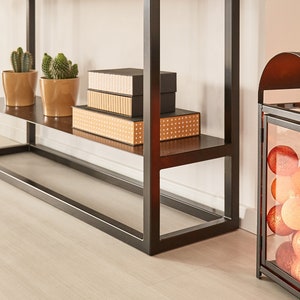 May include: A black metal lantern with a glass panel filled with orange and white cotton ball lights. The lantern is sitting on a wooden floor in front of a beige curtain.
