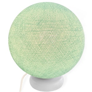 Pode incluir: Um abajur de mesa de bola de algod&atilde;o verde com uma base branca. A l&acirc;mpada est&aacute; acesa e emite um brilho quente.