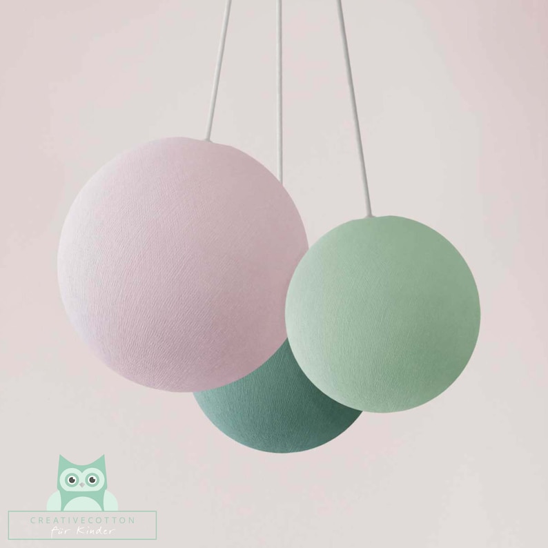 May include: Three hanging globe lights, one pink, one green, and one teal. The lights are made of fabric and have a soft, textured appearance.