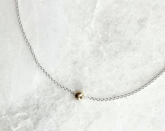 May include: A delicate silver chain necklace with a single gold bead pendant.