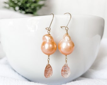 May include: A pair of gold earrings with peach-colored baroque pearls and teardrop-shaped sunstone accents.