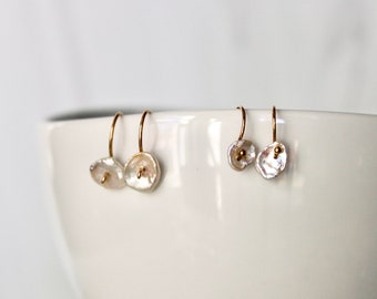 May include: A pair of gold hoop earrings with a white pearl charm. The earrings are displayed on a white surface.