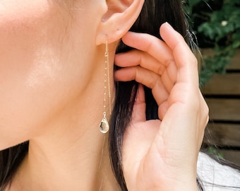 May include: A pair of gold chain earrings with a teardrop-shaped clear gemstone dangling from each chain.