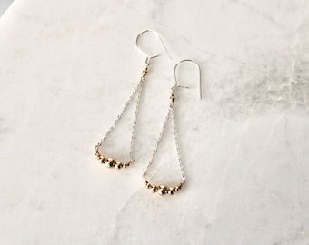 May include: A pair of silver dangle earrings with a curved row of gold beads at the bottom.